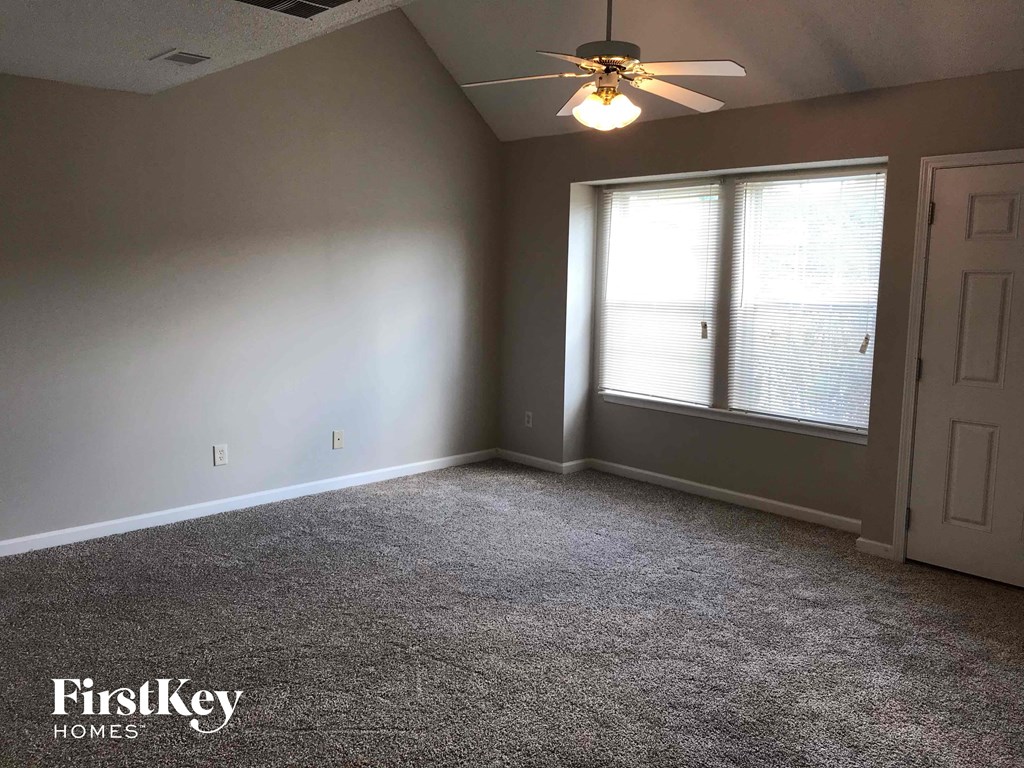 A room with a carpet floor, a ceiling fan, and a door.