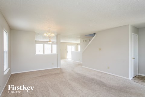 the living room and dining room of an apartment with carpet and white walls