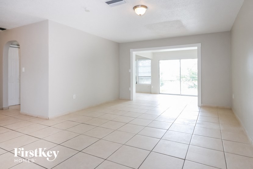 A spacious room with white tiled flooring and a sliding glass door leading to a balcony.