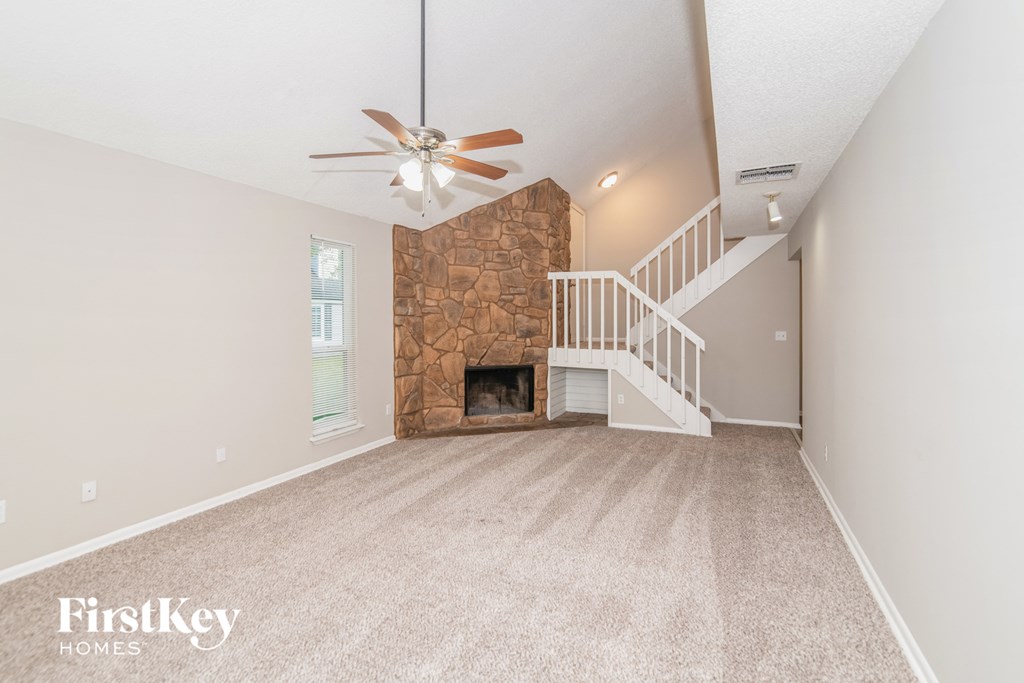 an empty living room with a stone fireplace and a ceiling fan