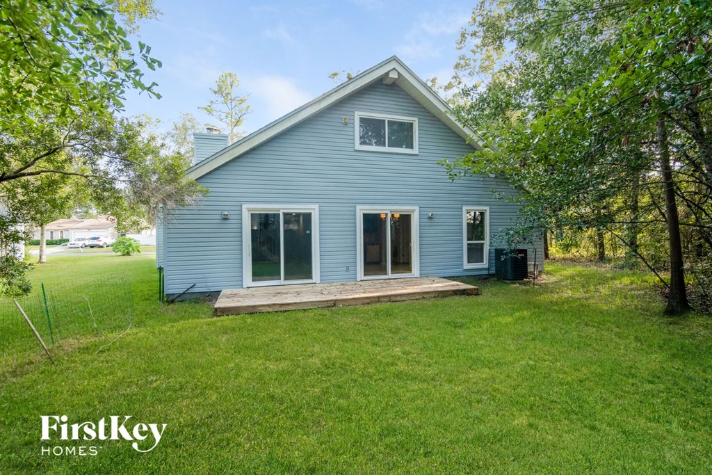 the back of a blue house with a lawn and trees
