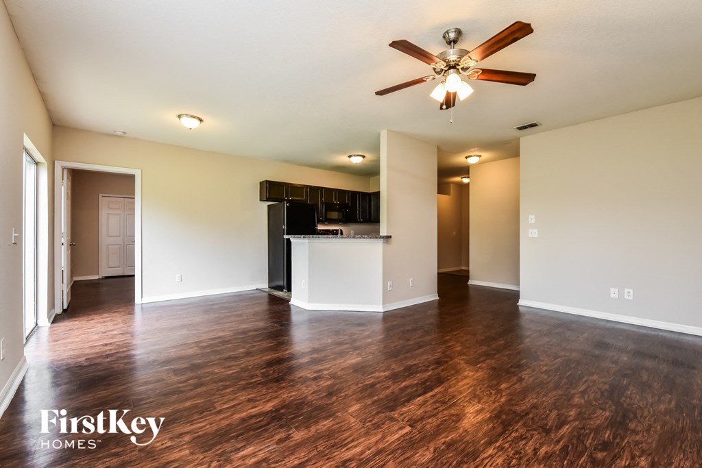 an empty living room with a ceiling fan and a kitchen