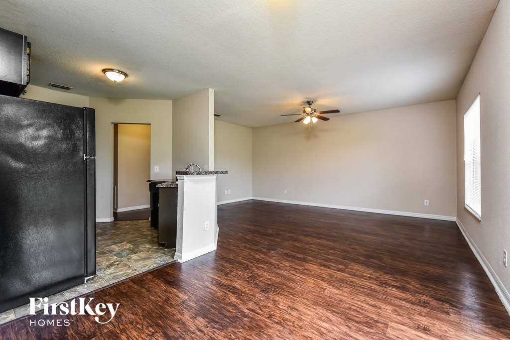 an empty living room with a kitchen and a ceiling fan
