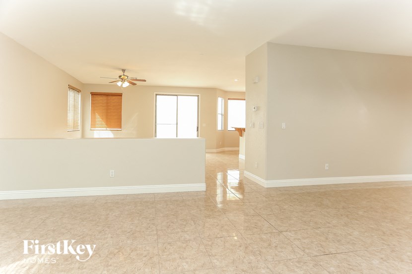 an empty living room with a kitchen and a ceiling fan