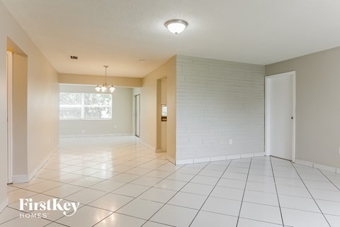 A spacious room with white tiled floors and a chandelier hanging from the ceiling.