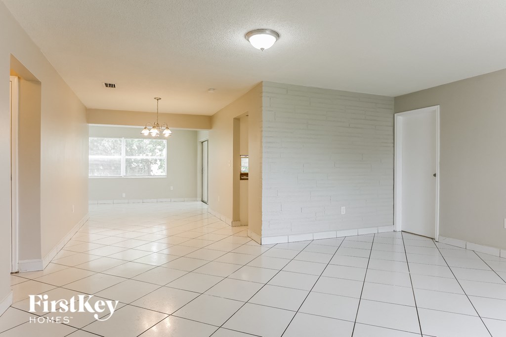 A spacious room with white tiled floors and a chandelier hanging from the ceiling.