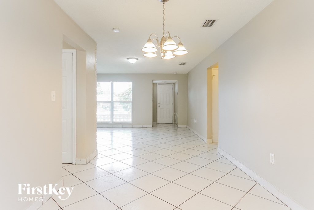 A spacious, empty room with white tile flooring and a chandelier hanging from the ceiling.