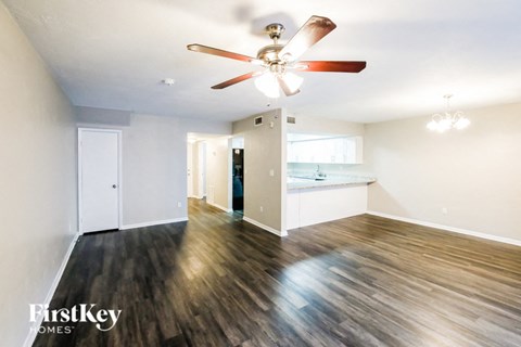 an empty living room with a ceiling fan and a kitchen