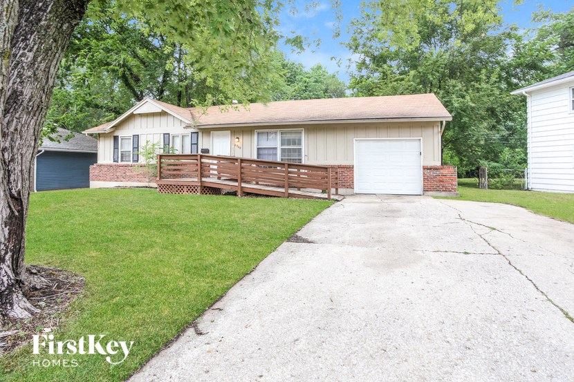 A house with a brown and white exterior is surrounded by greenery and has a white garage door.