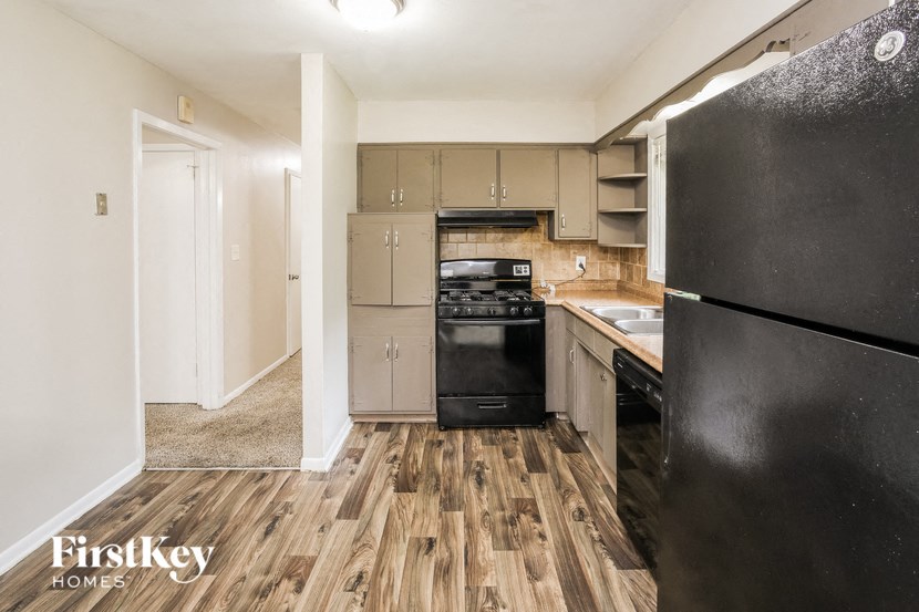 A kitchen with a black refrigerator, wooden floors, and a white wall.