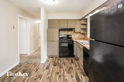 A kitchen with a black refrigerator, wooden floors, and a white wall.