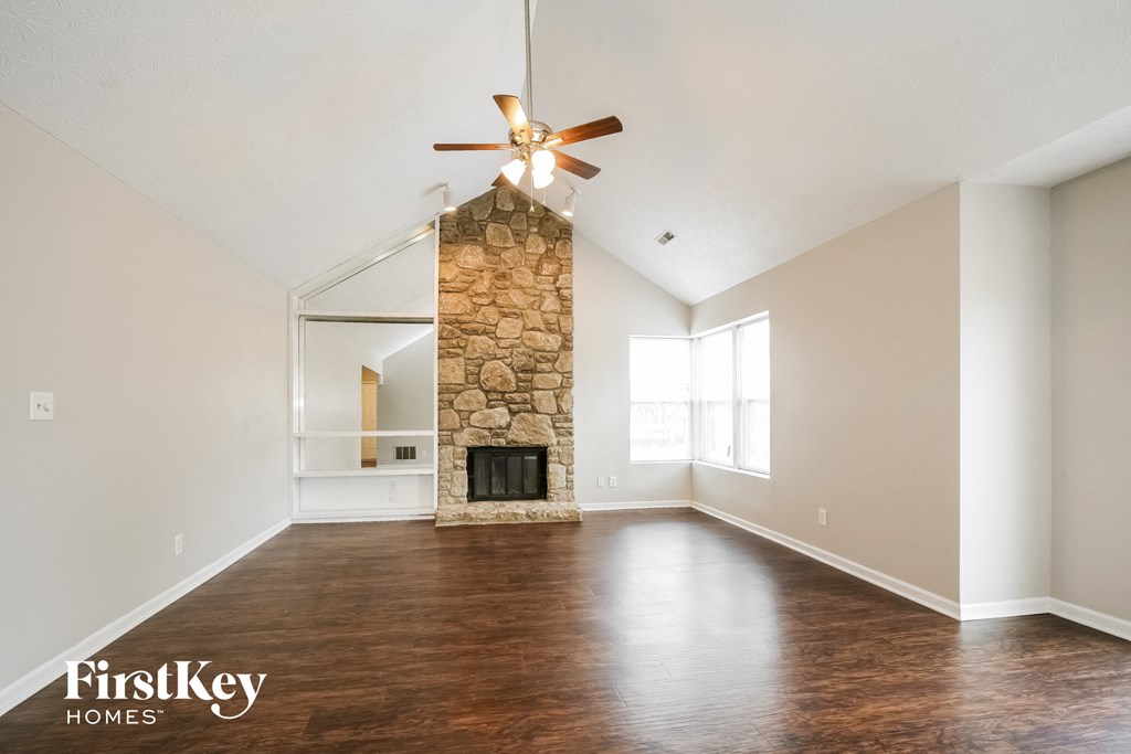 an empty living room with a stone fireplace and a ceiling fan