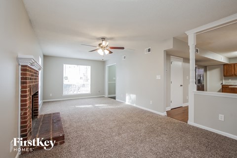 A spacious living room with a brick fireplace and a ceiling fan.