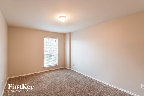 the upstairs bedroom has a large window and beige walls and carpet