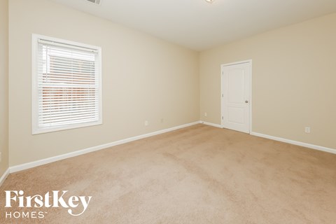a bedroom with beige carpet and a window and a white door