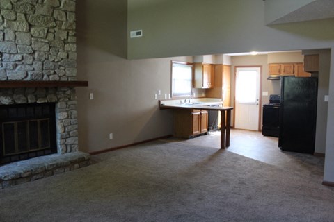 A kitchen with a black refrigerator and a stone fireplace.
