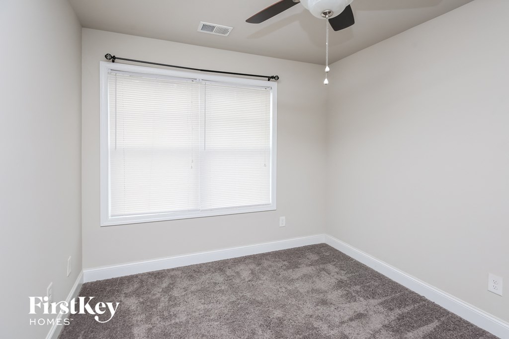 a carpeted room with a large window and a ceiling fan
