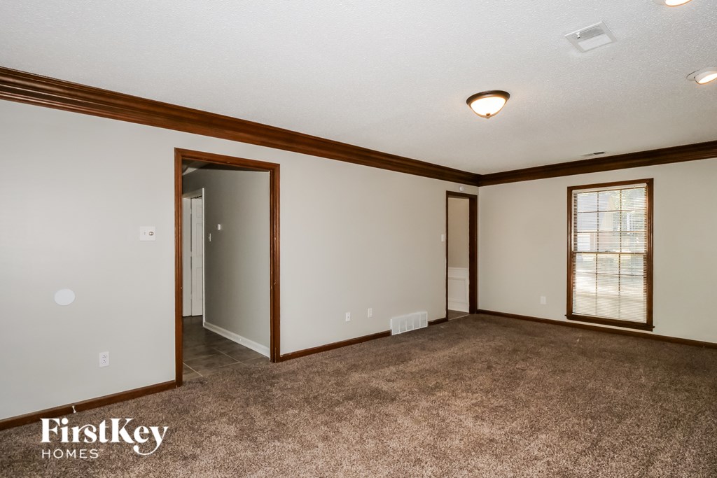 A room with a carpeted floor and a window with a wooden frame.