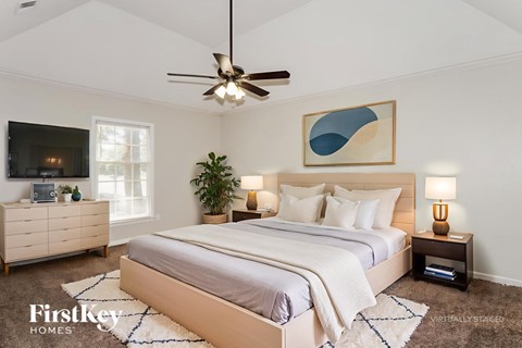 A bedroom with a large bed, a ceiling fan, and a dresser with a television on top.
