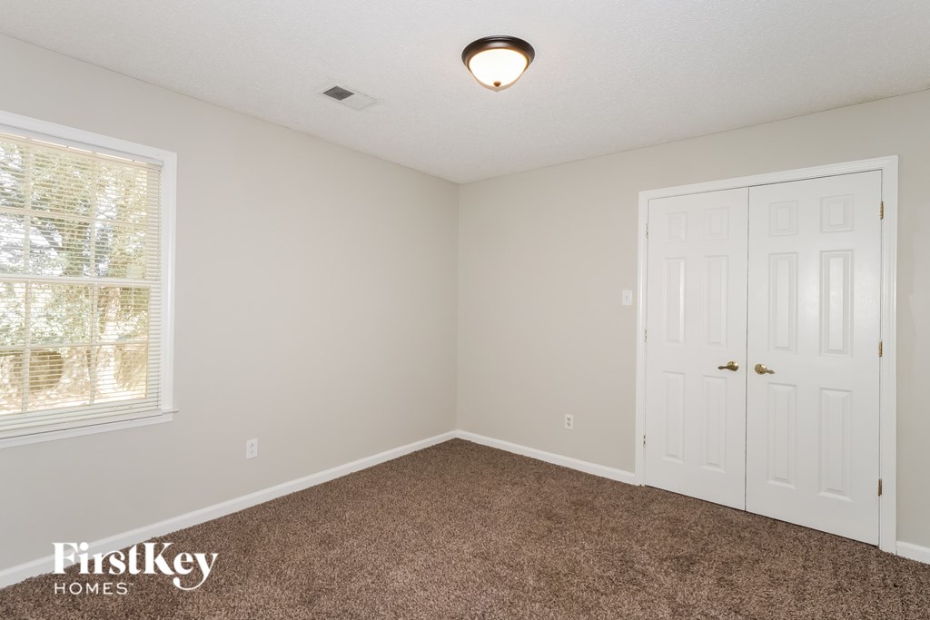 A room with a carpeted floor, a window with blinds, a door, and a ceiling light fixture.