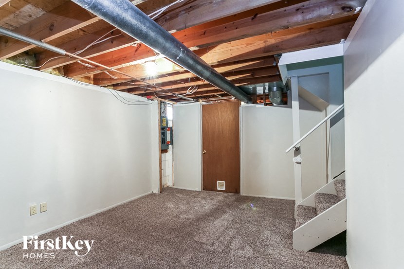 a basement with white walls and a staircase and a wood ceiling
