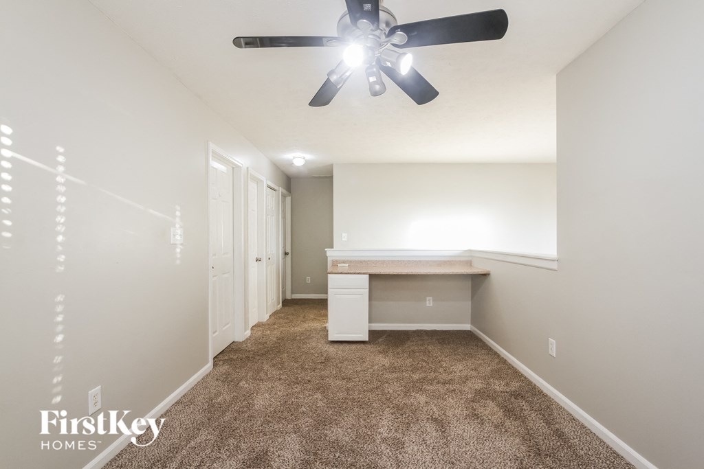 A carpeted room with a fan and a desk.