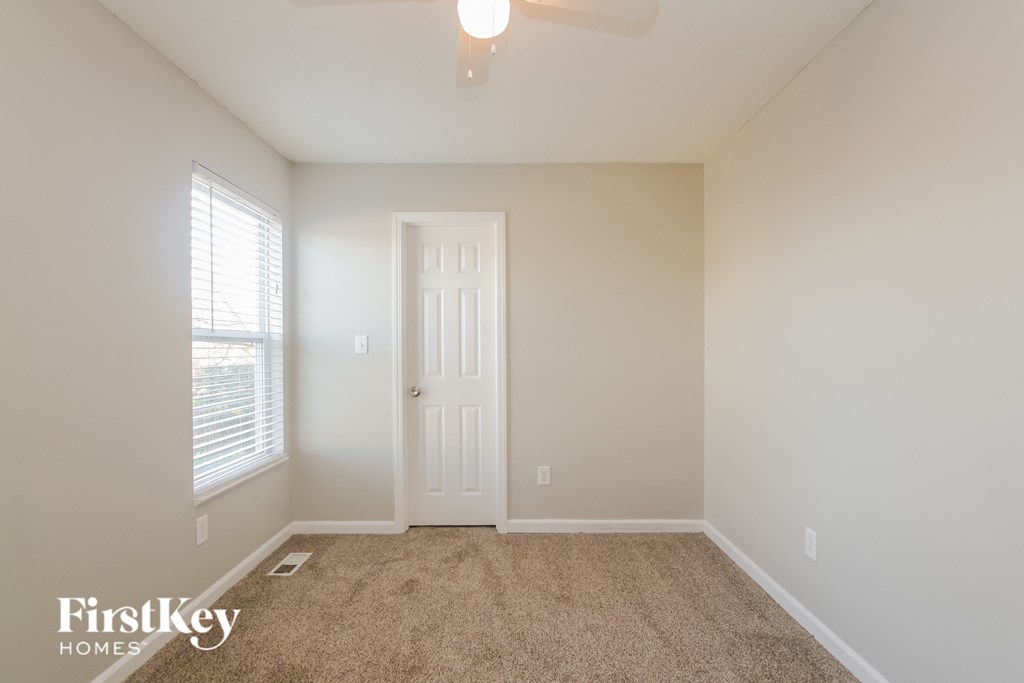 A room with a carpet floor, a ceiling fan, and a door.