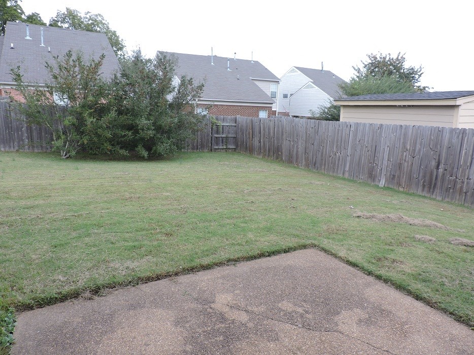 A backyard with a brown patch of dirt in the middle of the grass.