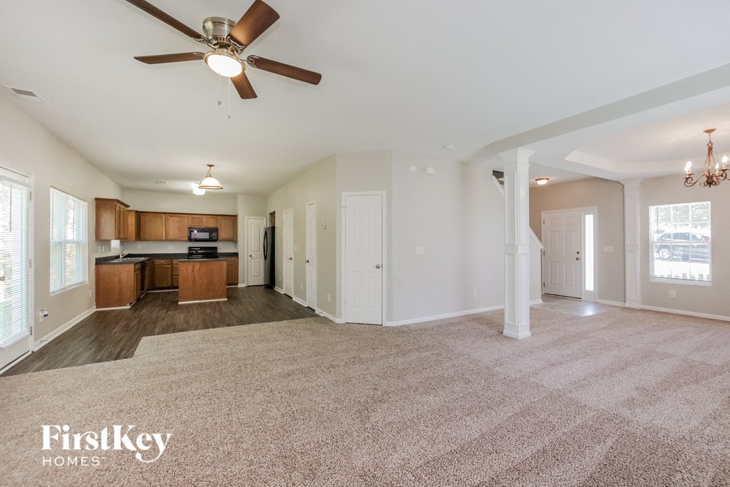 an empty living room with a ceiling fan and a kitchen