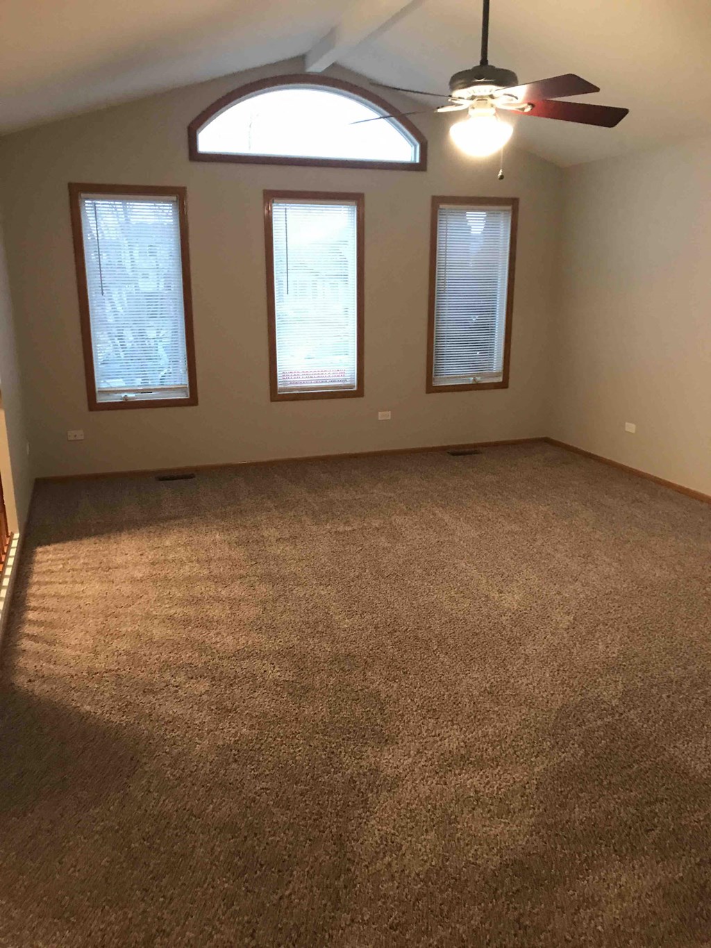 an empty living room with a ceiling fan and three windows
