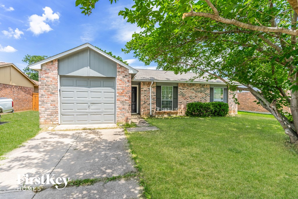 a small brick house with a gray garage door and a lawn