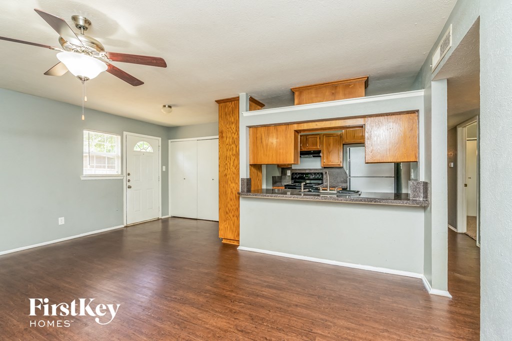 an empty living room with a kitchen and a ceiling fan