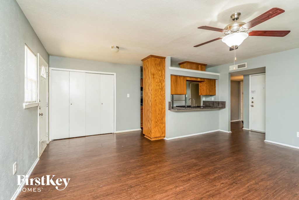 an empty living room and kitchen with wood flooring and a ceiling fan