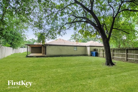 A tree stands in a grassy yard in front of a house.