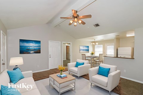 A living room with a ceiling fan and a painting of a beach scene on the wall.