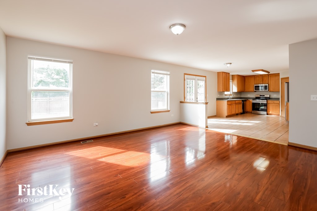 A spacious room with wooden floors and a kitchen in the background.