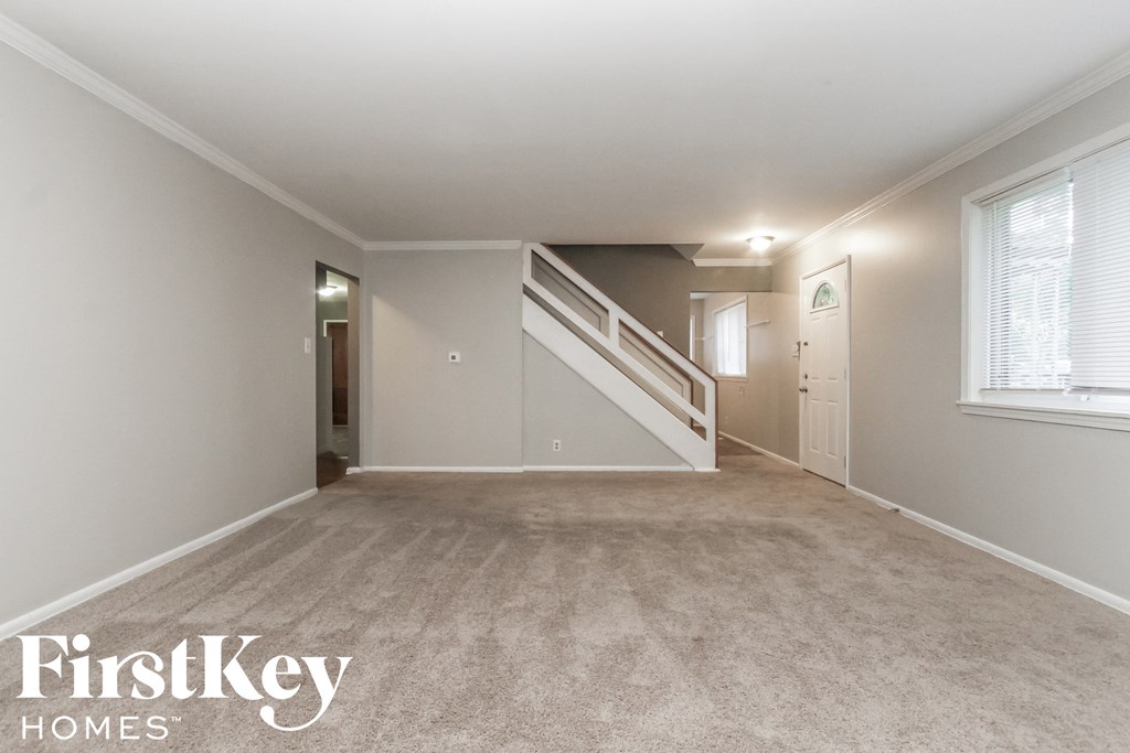a living room with a carpeted floor and a white staircase