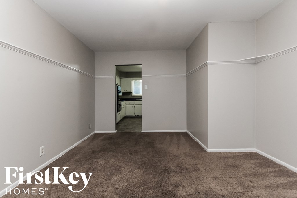 an empty living room with carpet and a kitchen in the background