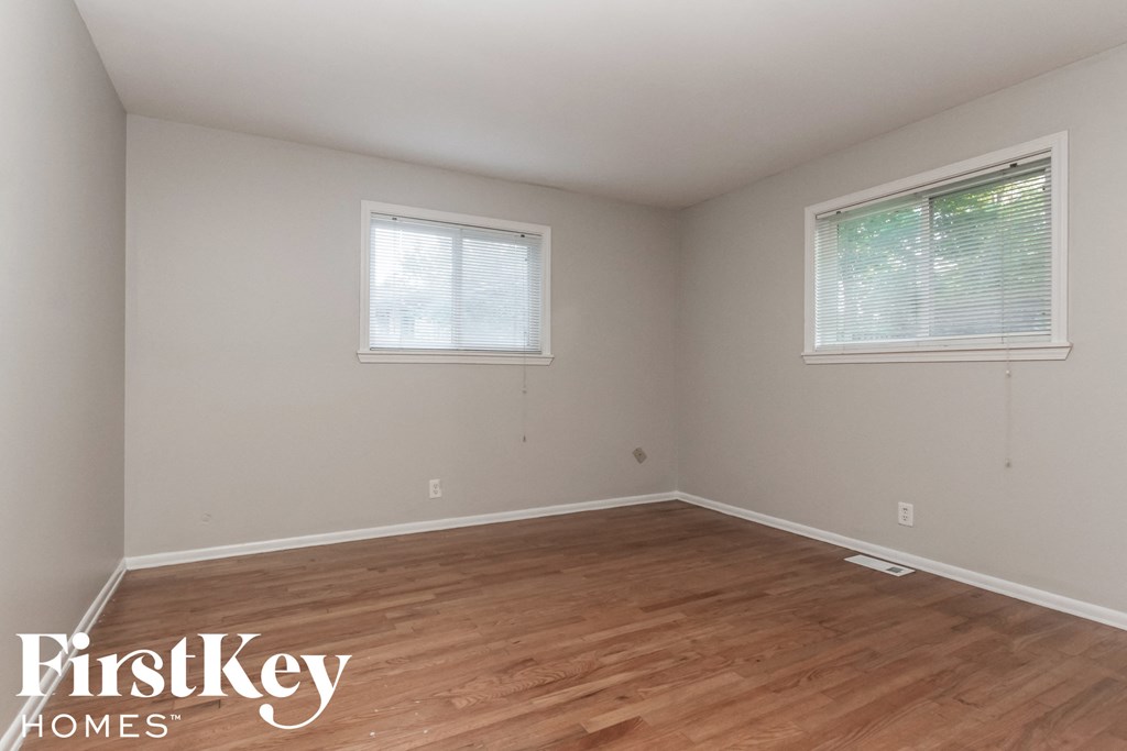 a bedroom with wood floors and white walls and two windows