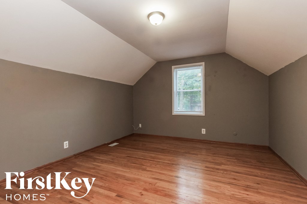 the attic of a home with wood flooring and a window