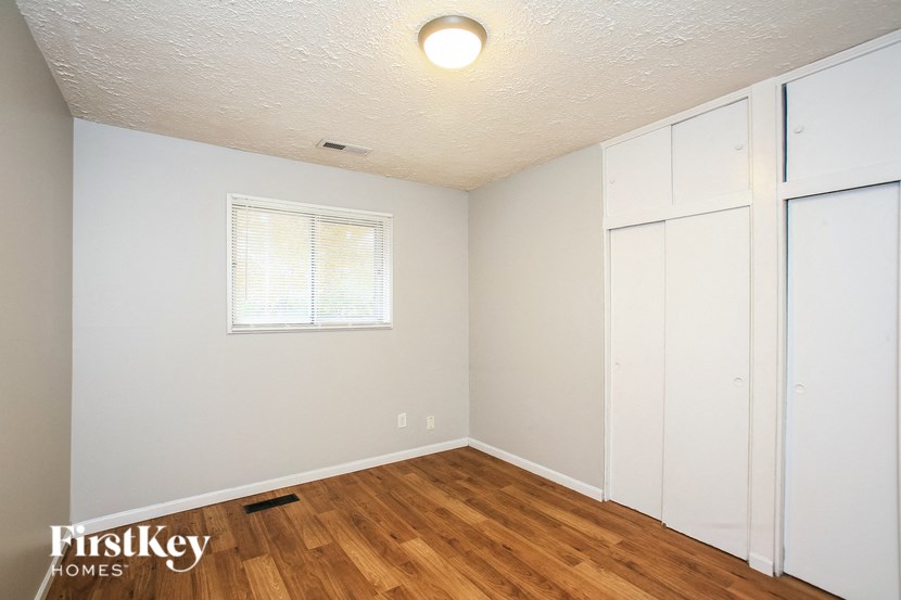 a bedroom with white cabinets and wood flooring and a window