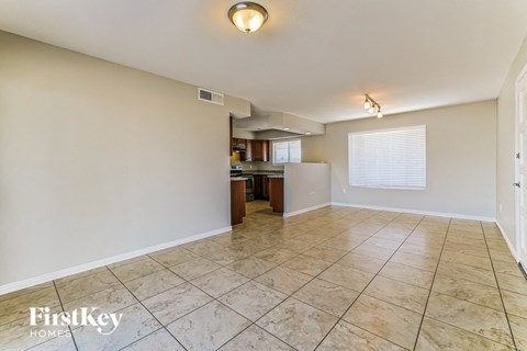an empty living room with a kitchen in the background