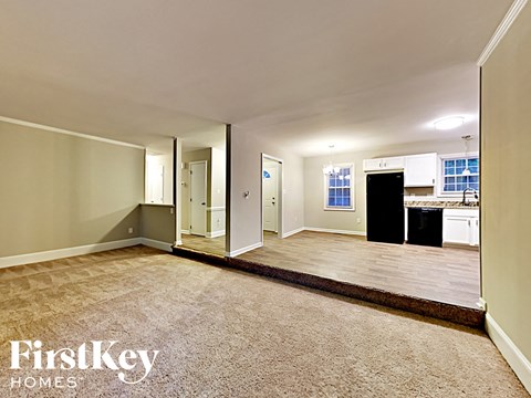 an empty living room with a kitchen in the background