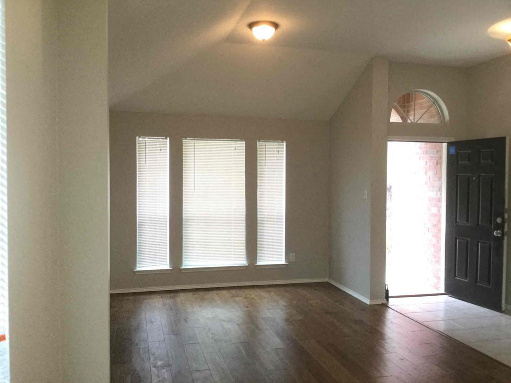 an empty living room with hard wood floors and windows