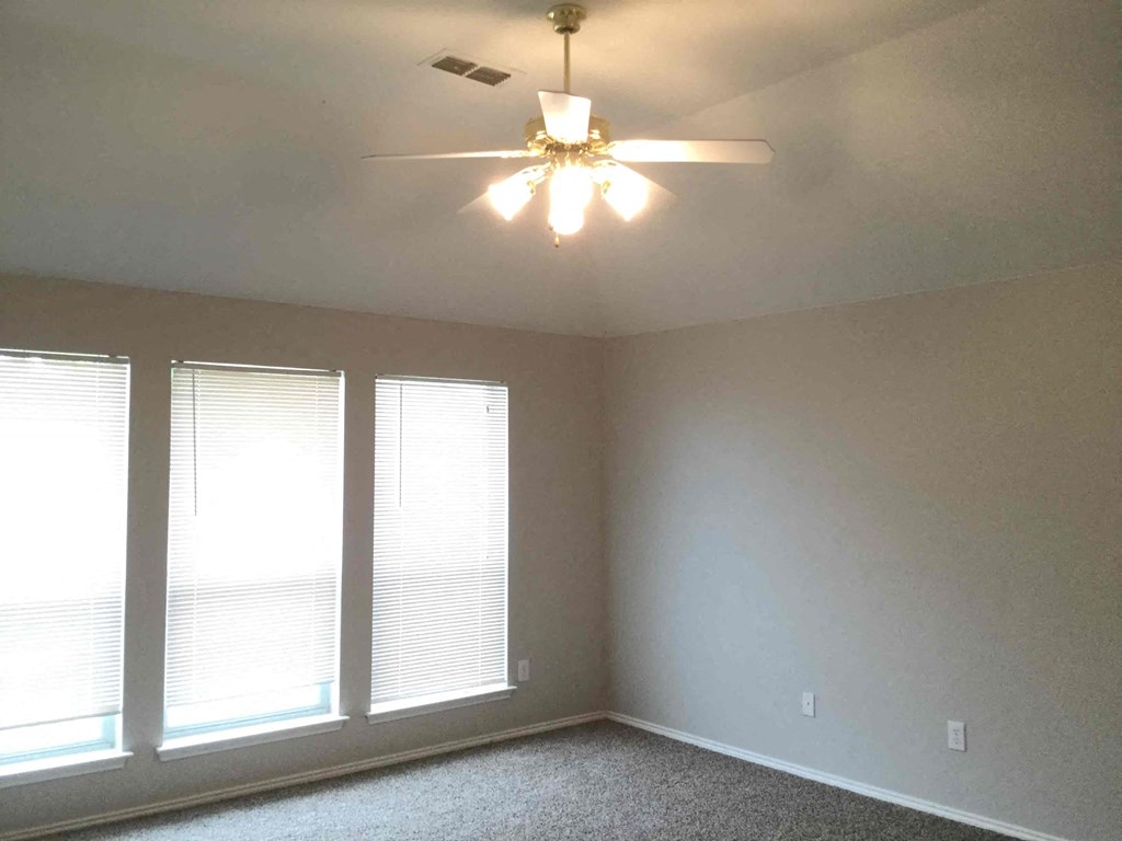 a living room with three windows and a ceiling fan