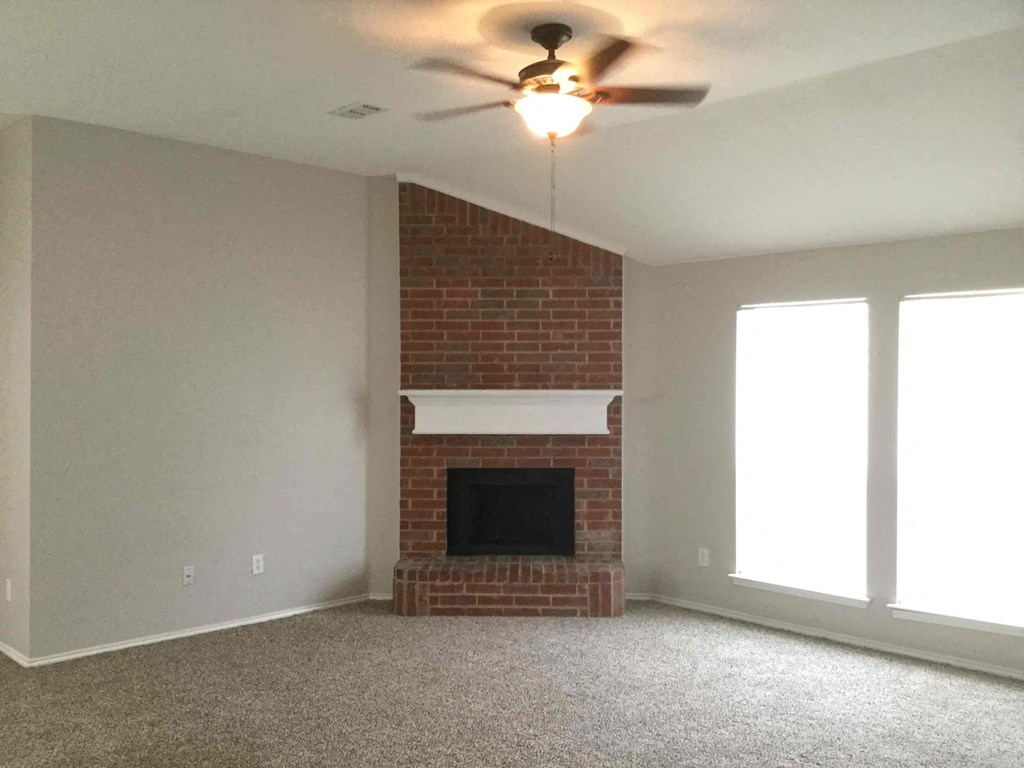 a living room with a brick fireplace and a ceiling fan