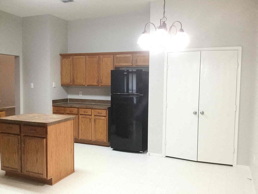 an empty kitchen with black refrigerator and wooden cabinets