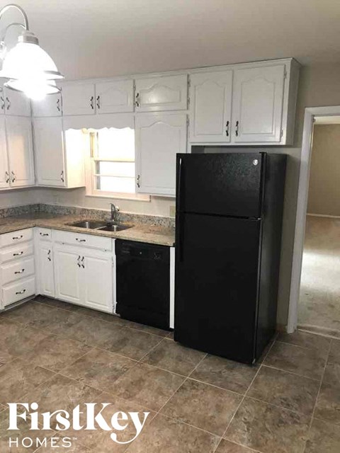 A black refrigerator stands in a kitchen with white cabinets.