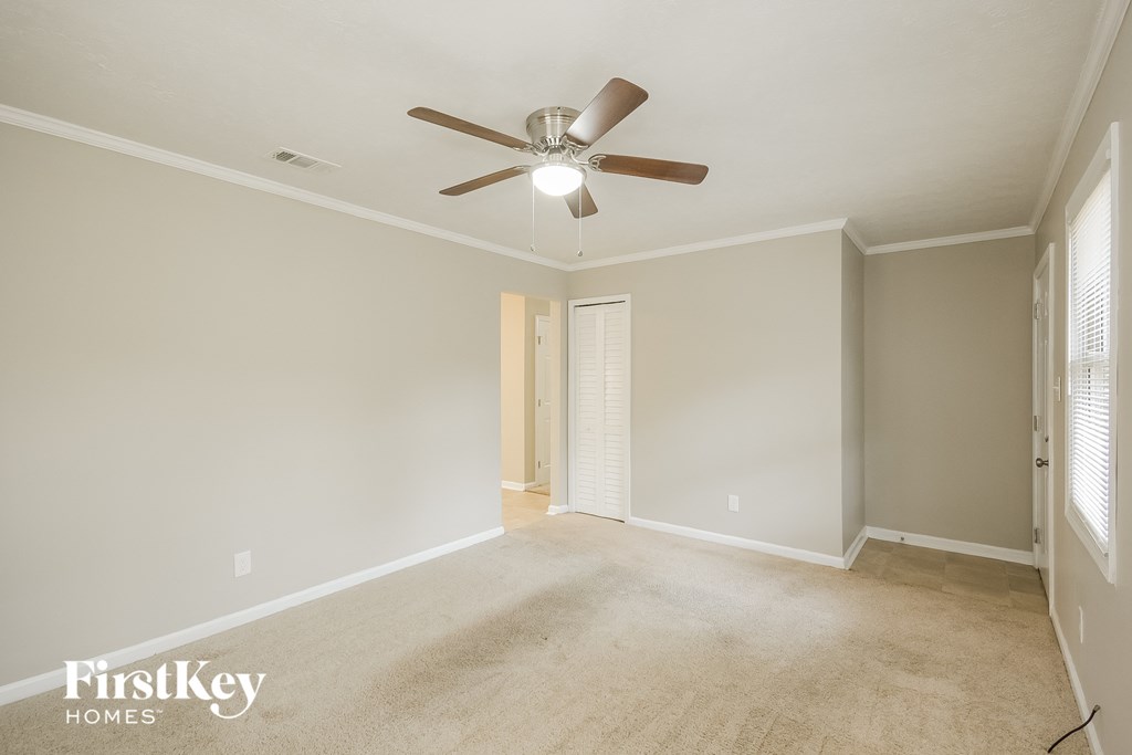 a empty living room with a ceiling fan and a door to a hallway
