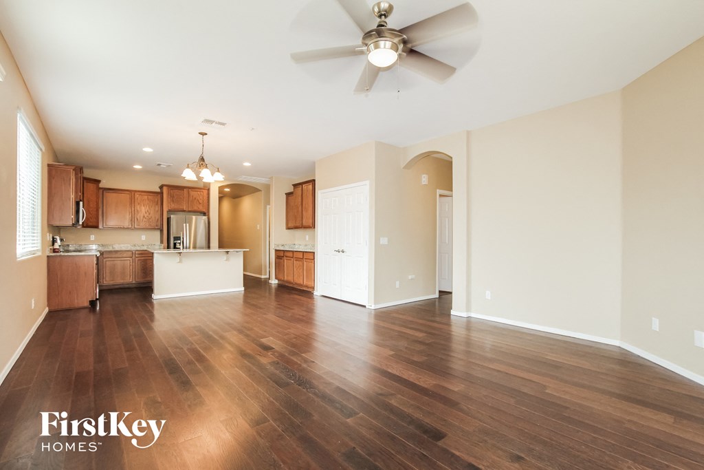 an empty living room and kitchen with wood flooring and a ceiling fan